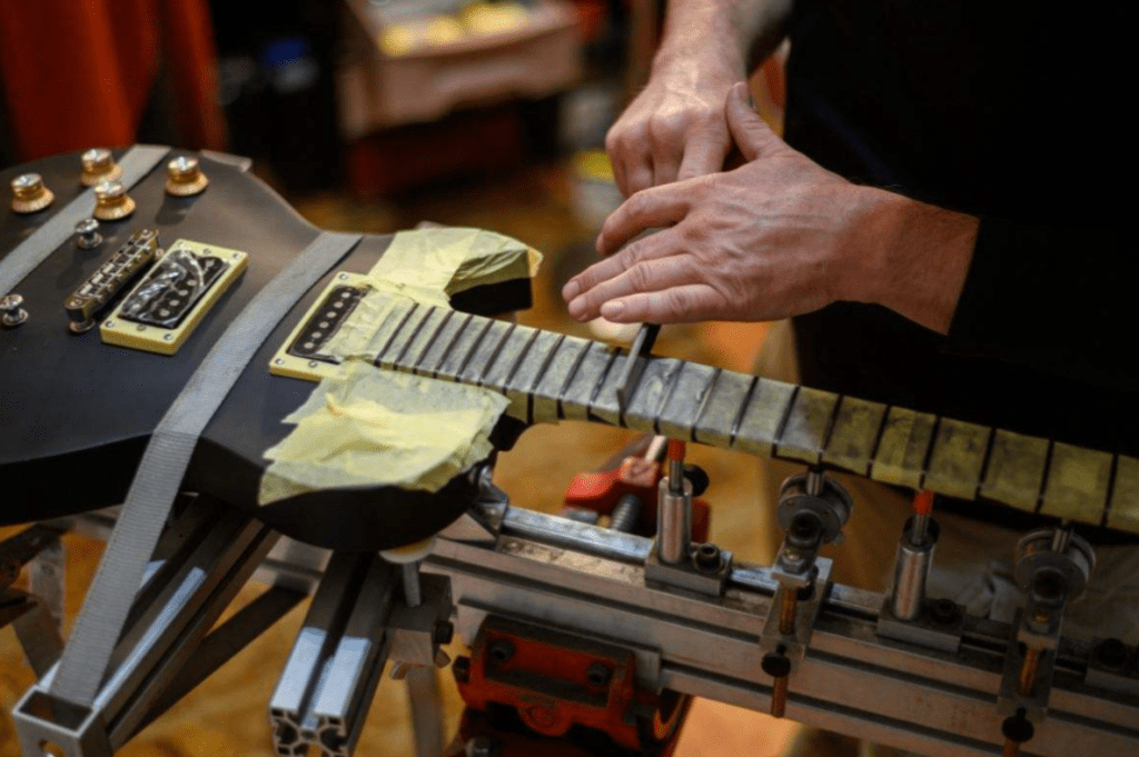 Luthier usando mesa de tensión StewMac para nivelar trastes de guitarra eléctrica 